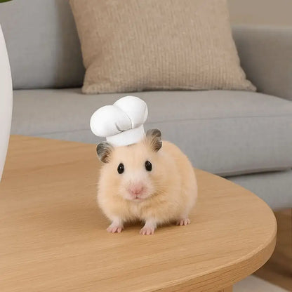 Hamster Chef Hat – Breathable Comfort All Day Wear + Adjustable Fit For Plush Ears on a light brown hamster wearing a small white chef hat on a wooden table