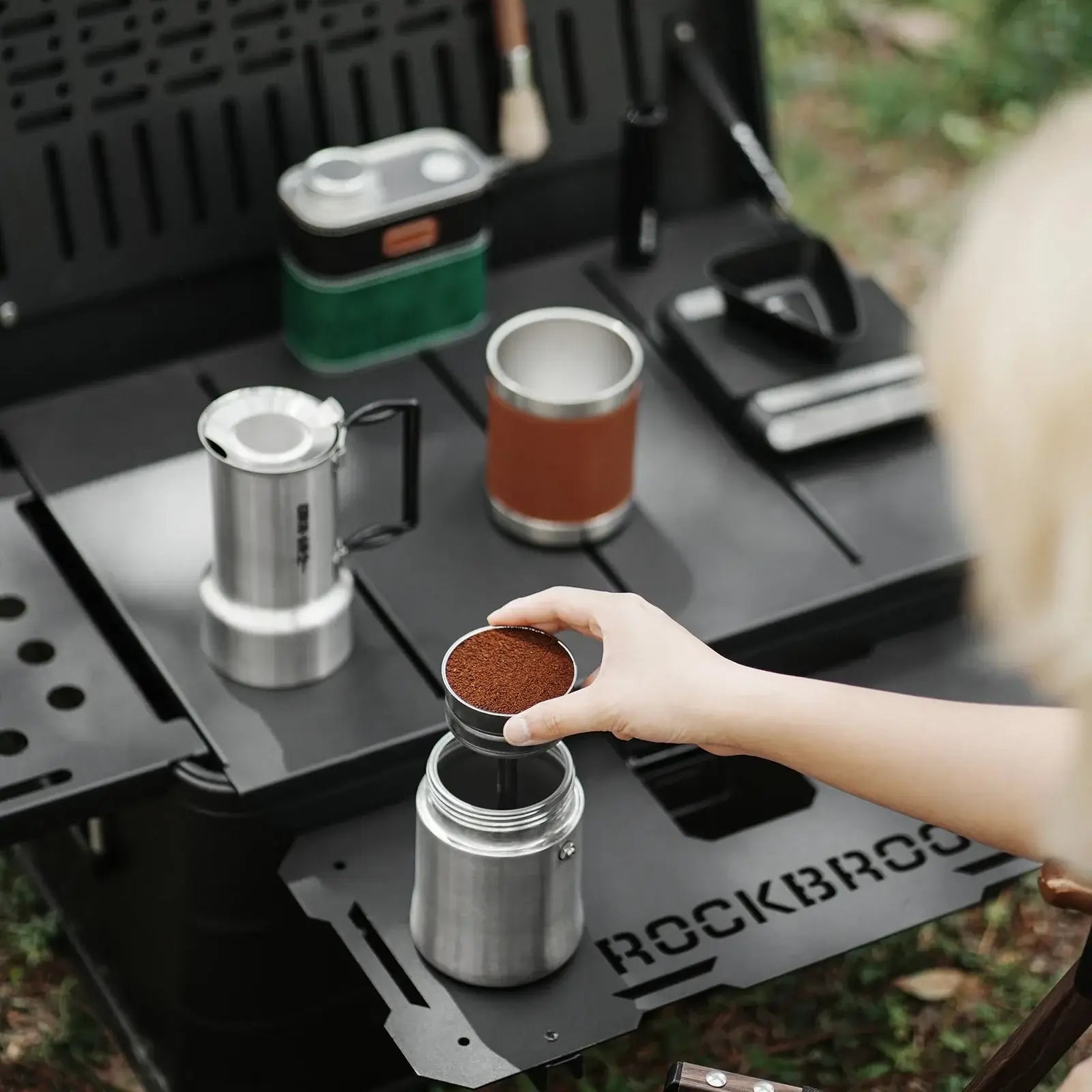 Stainless Steel Moka Pot – Rich Coffee + Foldable Handle shown brewing moka coffee outdoors with grounds and foldable handle
