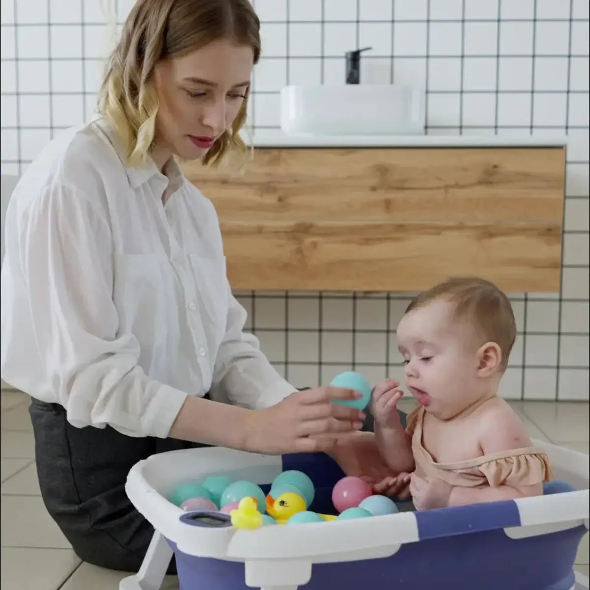 Parent playing with baby in a foldable newborn baby bath tub filled with colorful toys.